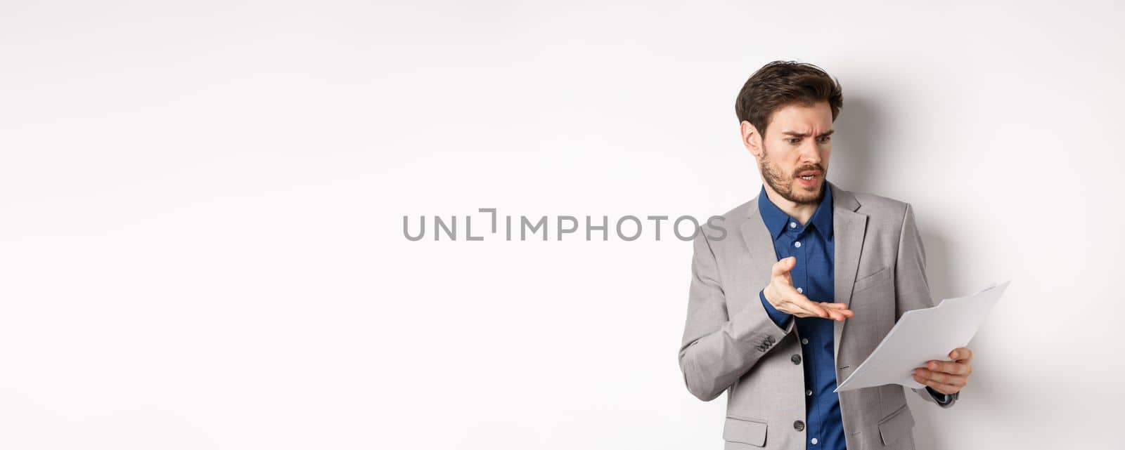 Angry employer looking at bad document, complaining on deal, pointing at paper frustrated, standing in suit on white background.
