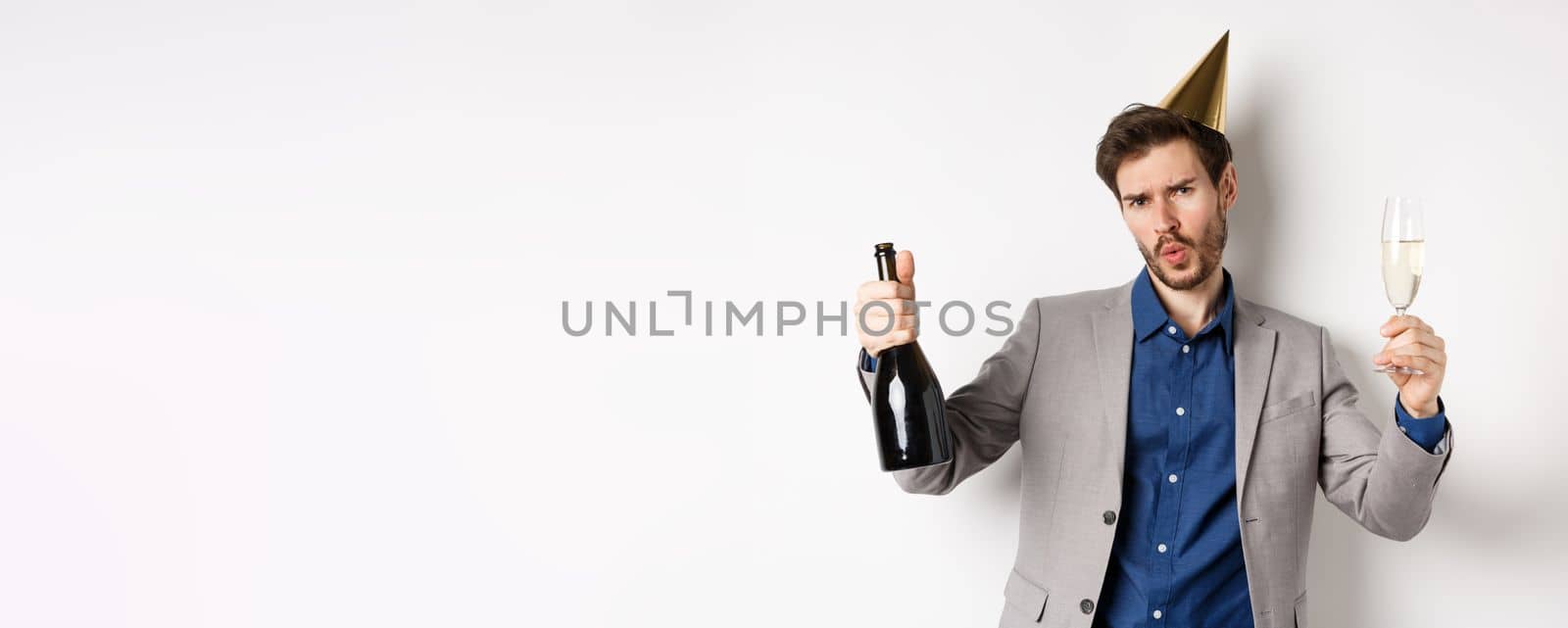 Celebration and holidays concept. Happy man in suit having fun at party, wearing birthday hat, dancing with champagne and drinking alcohol.