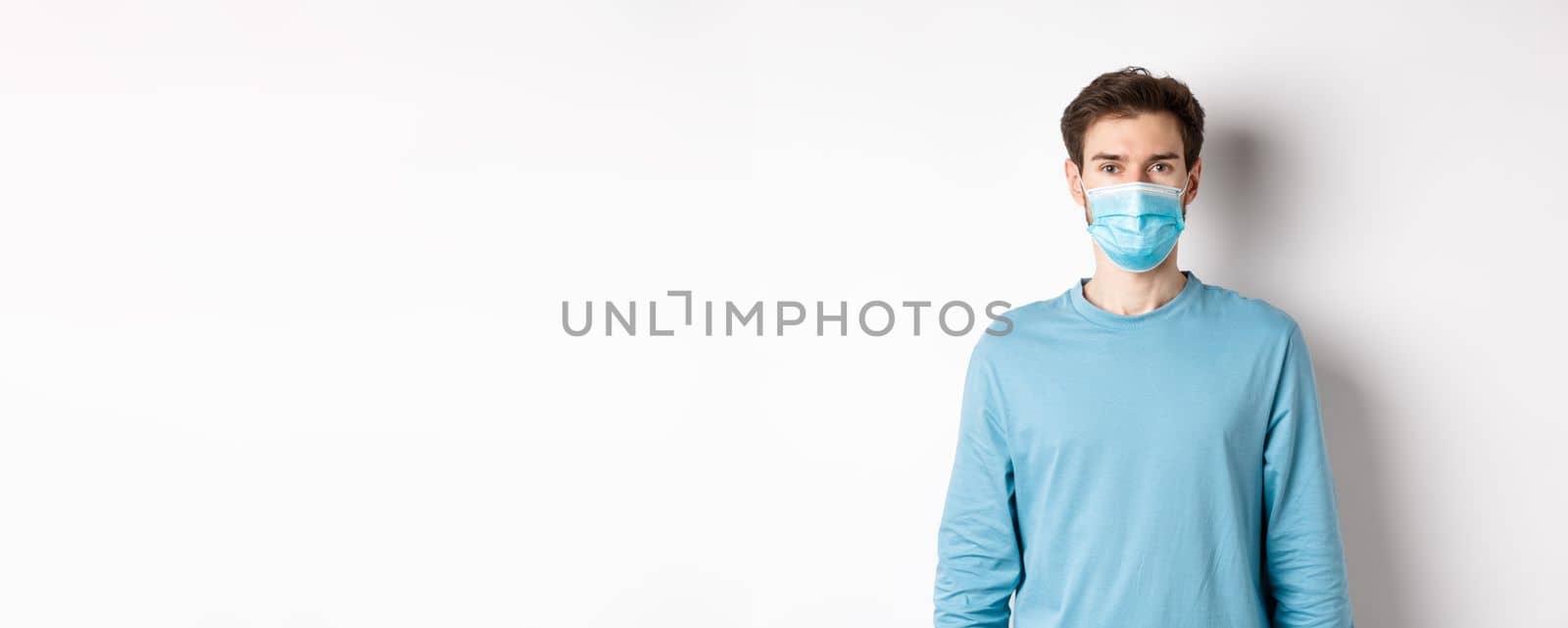 Covid-19, pandemic and social distancing concept. Young man wearing medical mask from coronavirus, standing over white background.