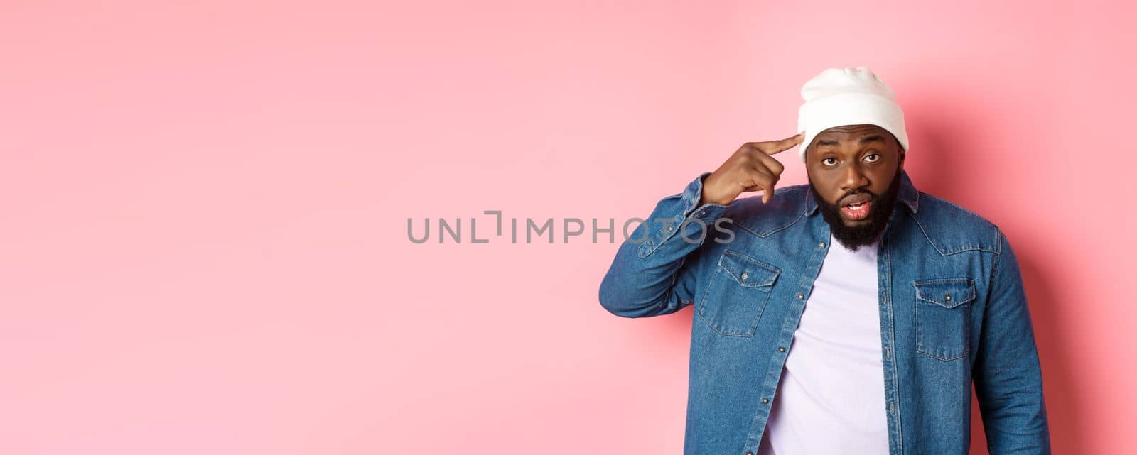 Annoyed and pissed-off african-american man pointing finger at head, scolding someone stupid, staring bothered at camera, pink background by Benzoix