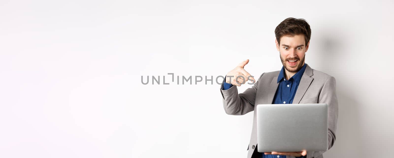 Excited male ceo manager looking and pointing at laptop with amazed smile, checking out special deal online, standing on white background.