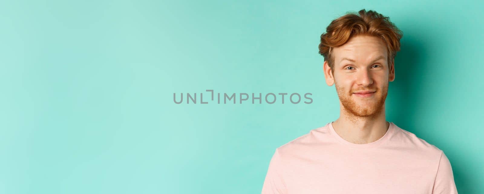 Close up of redhead bearded man looking pleased, nod in approval and smiling, standing in pink t-shirt against turquoise background by Benzoix