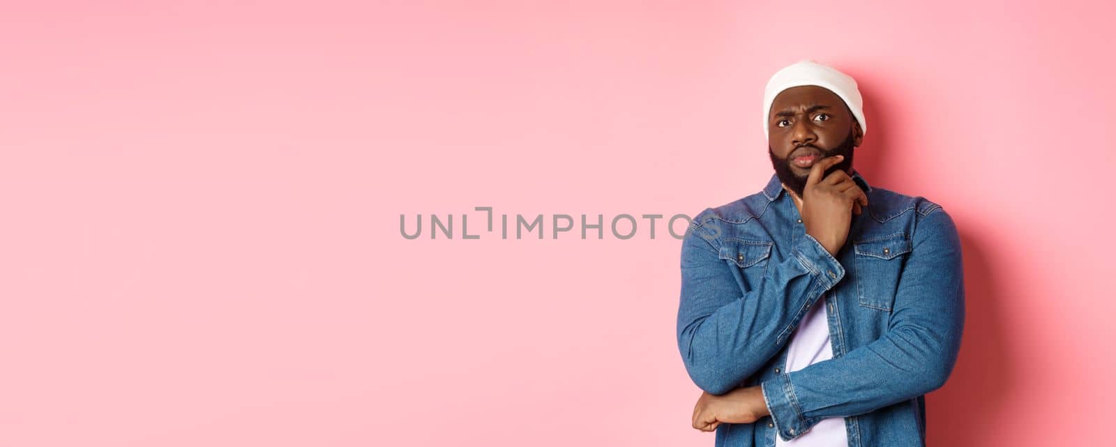 Doubtful african american man staring at camera with disbelief, standing skeptical and thinking, pink background.