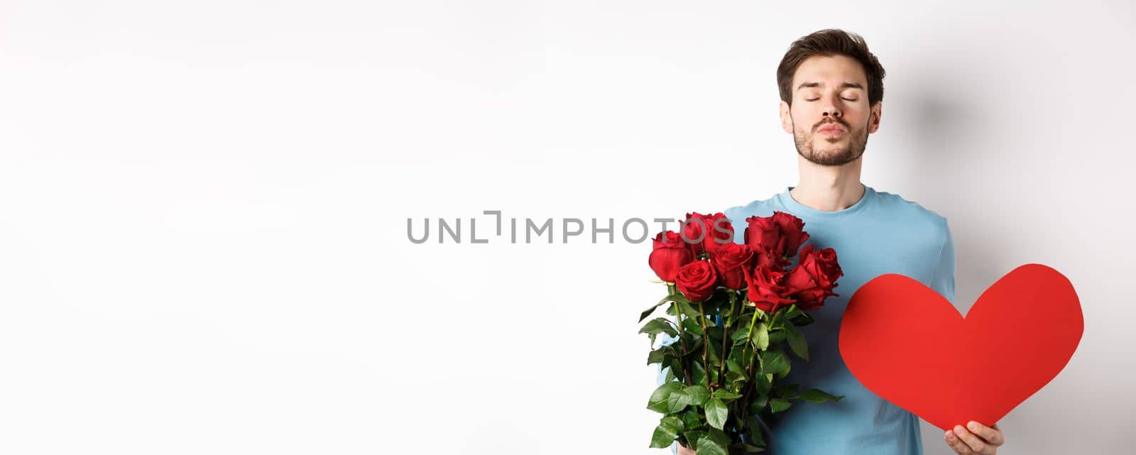 Romantic boyfriend waiting for kiss, holding bouquet of roses flowers and big red heart on Valentines day, love in air, standing over white background by Benzoix