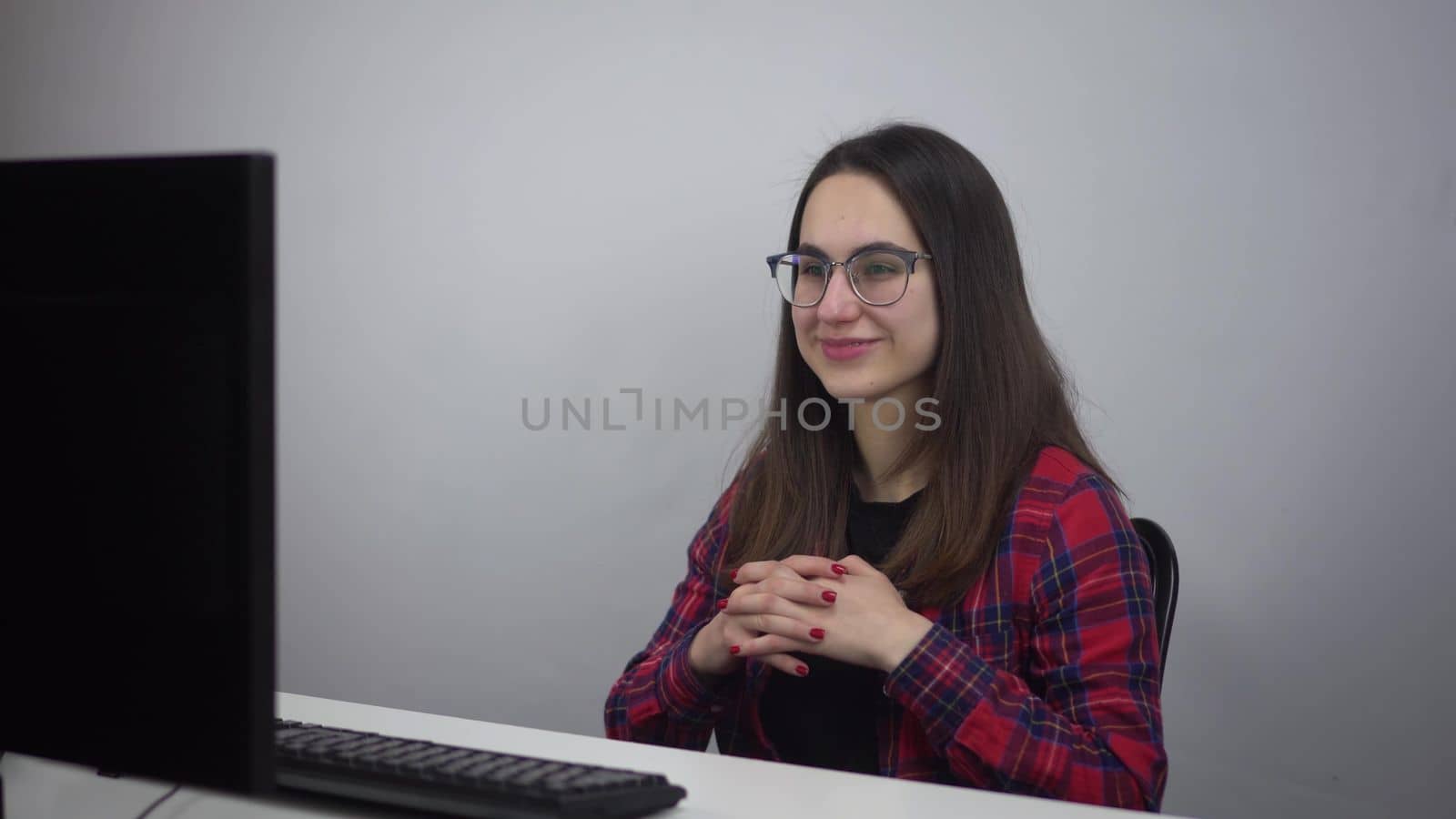 A young woman is talking on a video link while sitting in the office in front of a pc. Aichi specialist in glasses and a red shirt. 4k