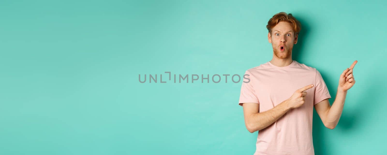 Handsome caucasian man with red hair, gasping in awe, pointing fingers at upper right corner, checking out promotion deal, standing over turquoise background by Benzoix