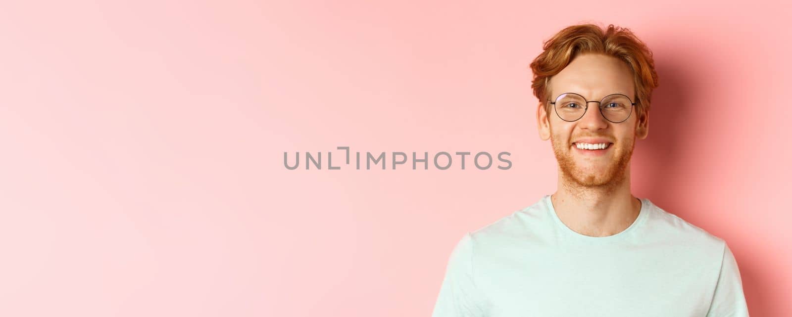 Close up of happy redhead man face, smiling with white teeth at camera, wearing glasses for better sight and t-shirt, standing over pink background by Benzoix