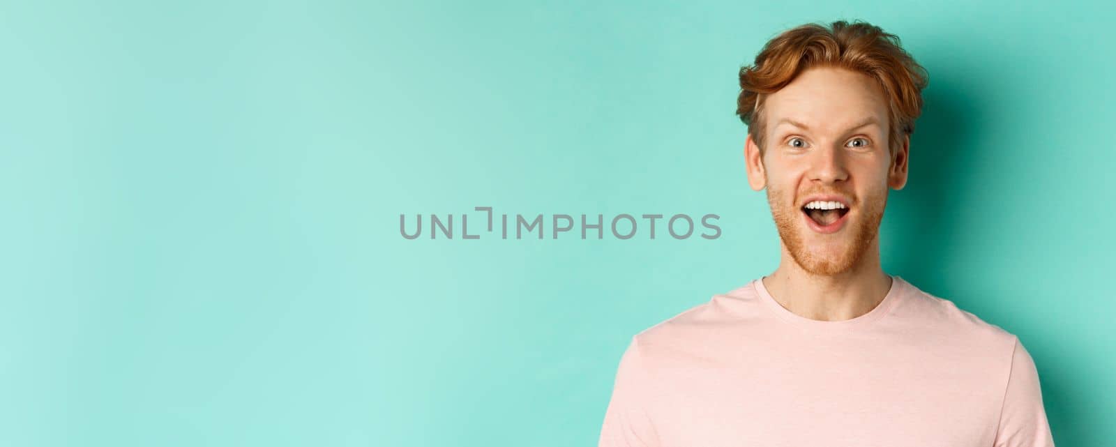 Close up of redhead bearded man raising eyebrows and looking surprised at camera, checking out promotion, standing over mint background.