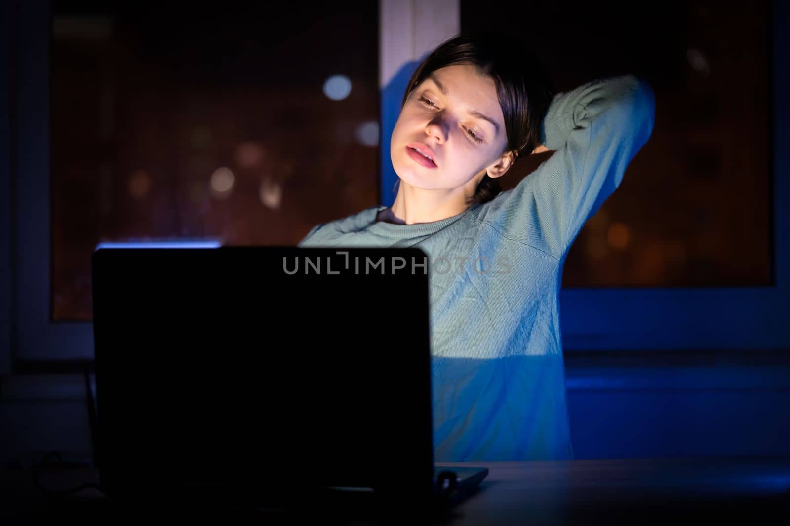 A young girl works while sitting at a laptop at night at home online, a woman is looking for information, texting, chatting using device via internet.