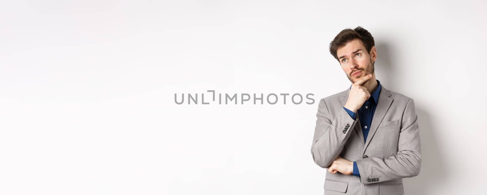 Thoughtful businessman in grey suit look at upper left corner logo, thinking or making choice, pondering plan, standing against white background.
