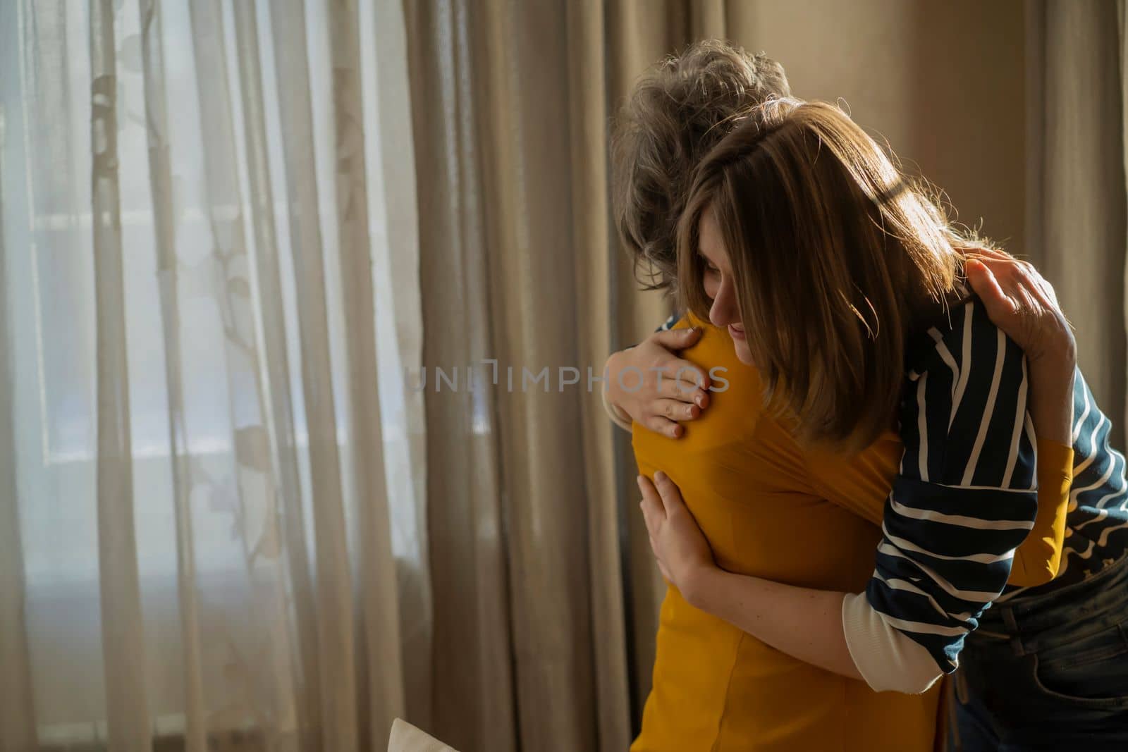 A young girl gently hugs her elderly mother or grandmother, visits her and supports in her cozy home, daughter takes care and congratulates her relative on the holiday.
