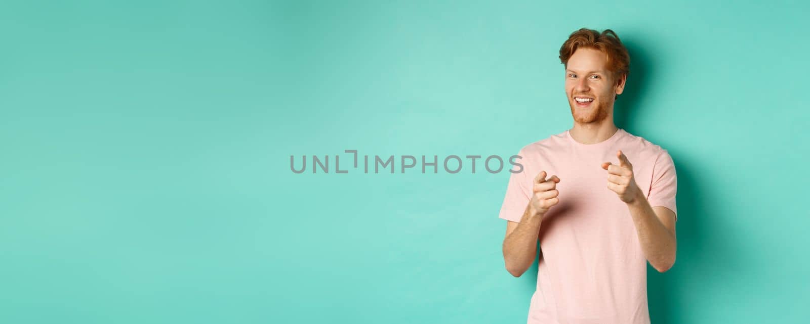 Funny redhead guy congratulating you, pointing fingers at camera and smiling, making choice, standing in t-shirt over mint background by Benzoix