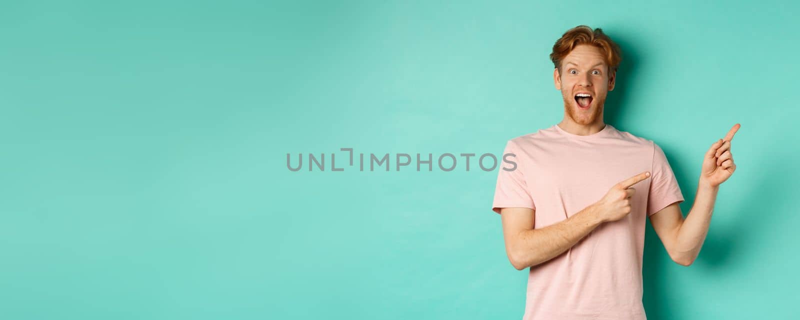 Excited guy in pink t-shirt showing advertisement on mint background, looking amazed at camera and pointing at upper right corner by Benzoix