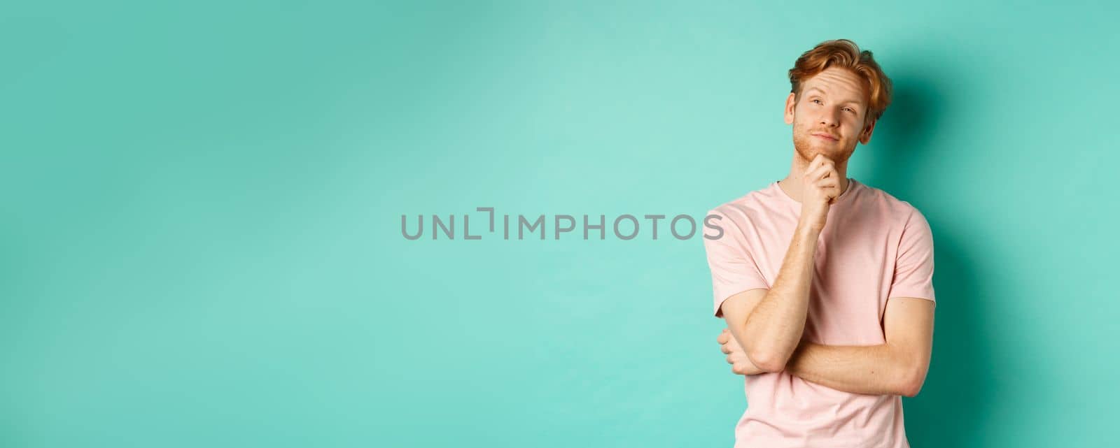 Pensive handsome man with red hair and beard looking at upper left corner, making choice and looking thoughtful, standing in t-shirt over mint background by Benzoix