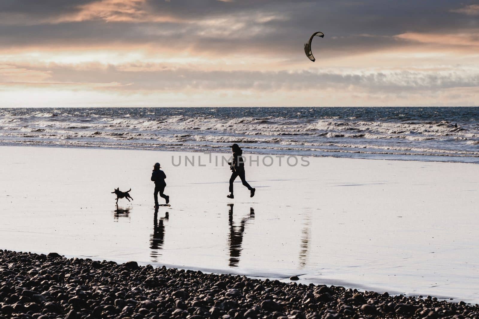 Mother daughter and dog running on the ocean coast at a sunset Selective focus