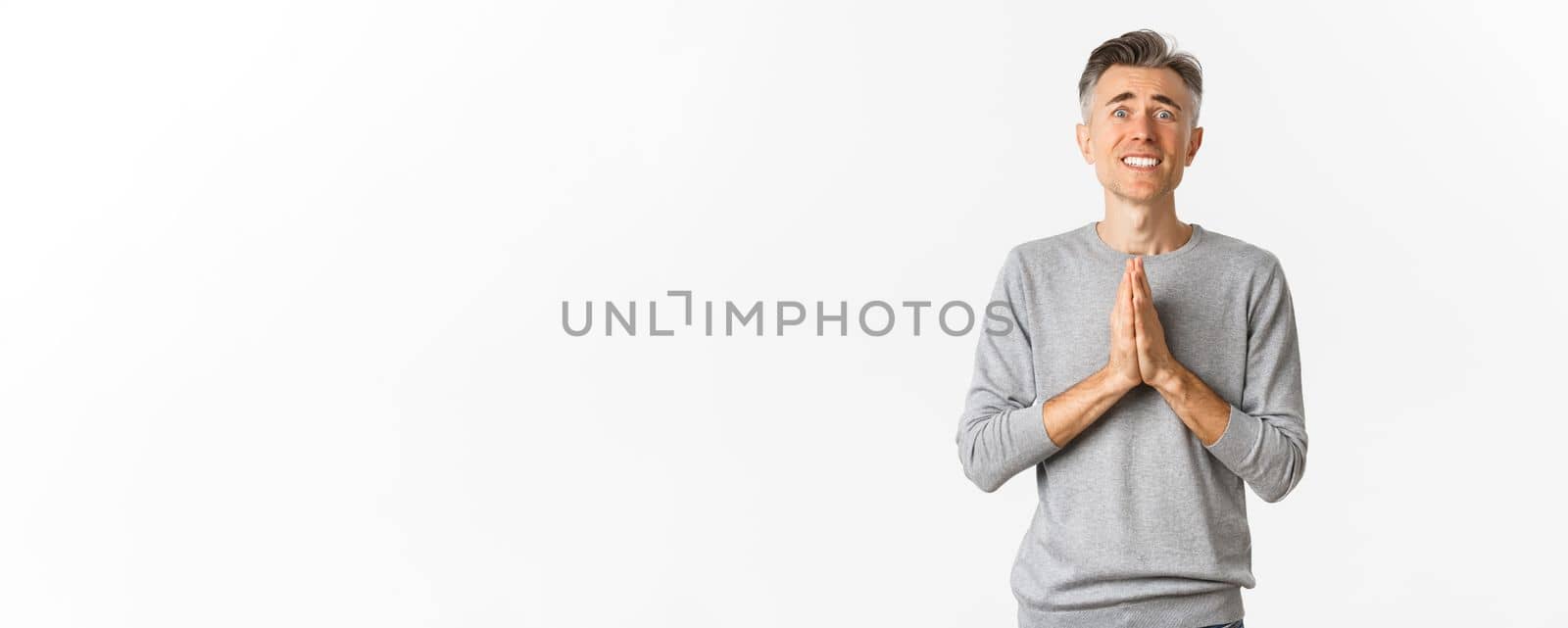 Image of nervous and desperate middle-aged man begging for help, holding hands in pray and looking worried, need favour, standing over white background.