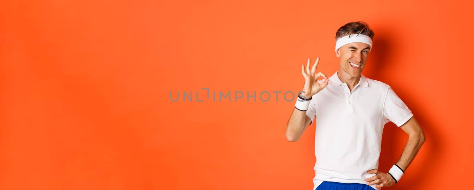 Concept of sport, fitness and lifestyle. Portrait of confident middle-aged sportsman, showing okay sign and look pleased, guarantee something or recommending gym, orange background.