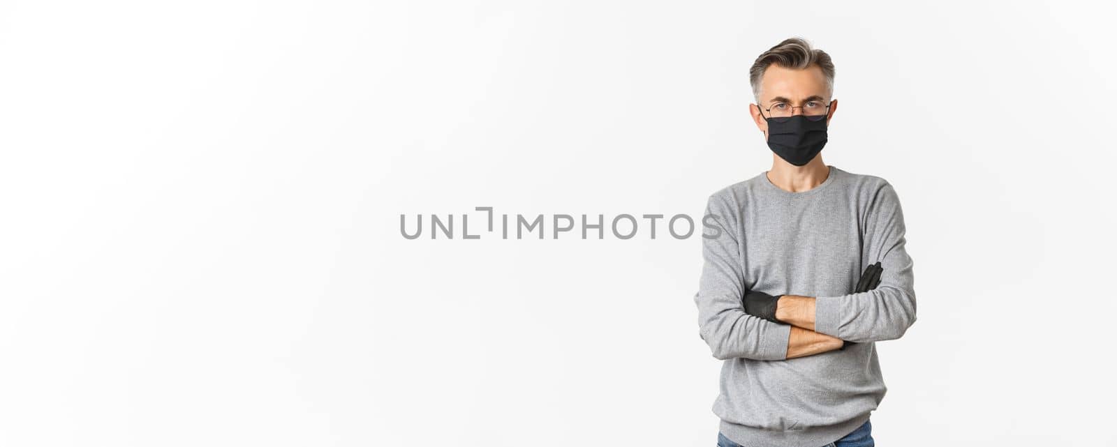 Concept of coronavirus, lifestyle and quarantine. Portrait of displeased middle-aged man in medical mask and gloves, cross arms on chest and looking disappointed, standing over white background.