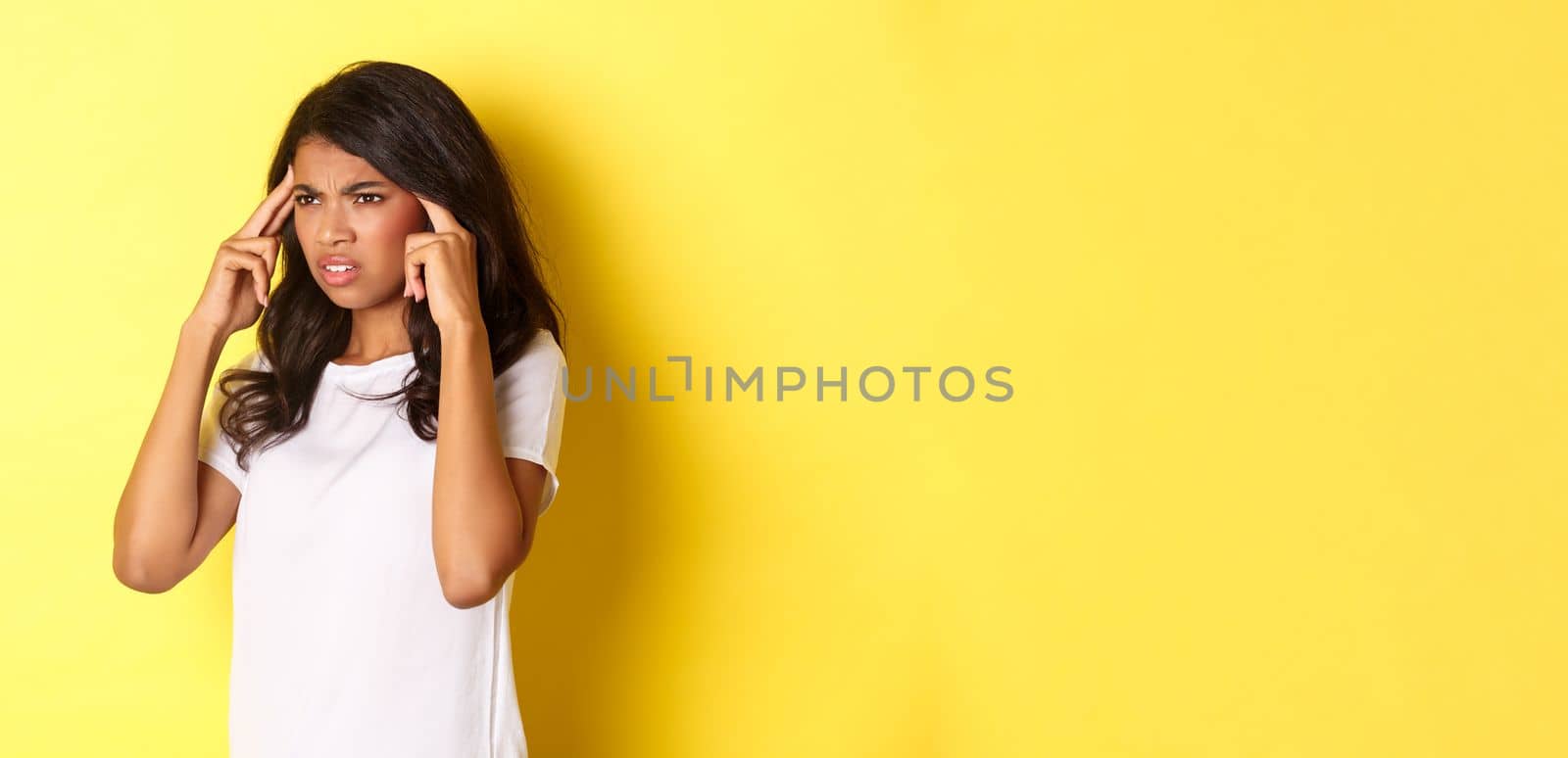 Portrait of troubled african-american woman cant think straight, touching head and grimacing, trying to remember and looking left, standing over yellow background.