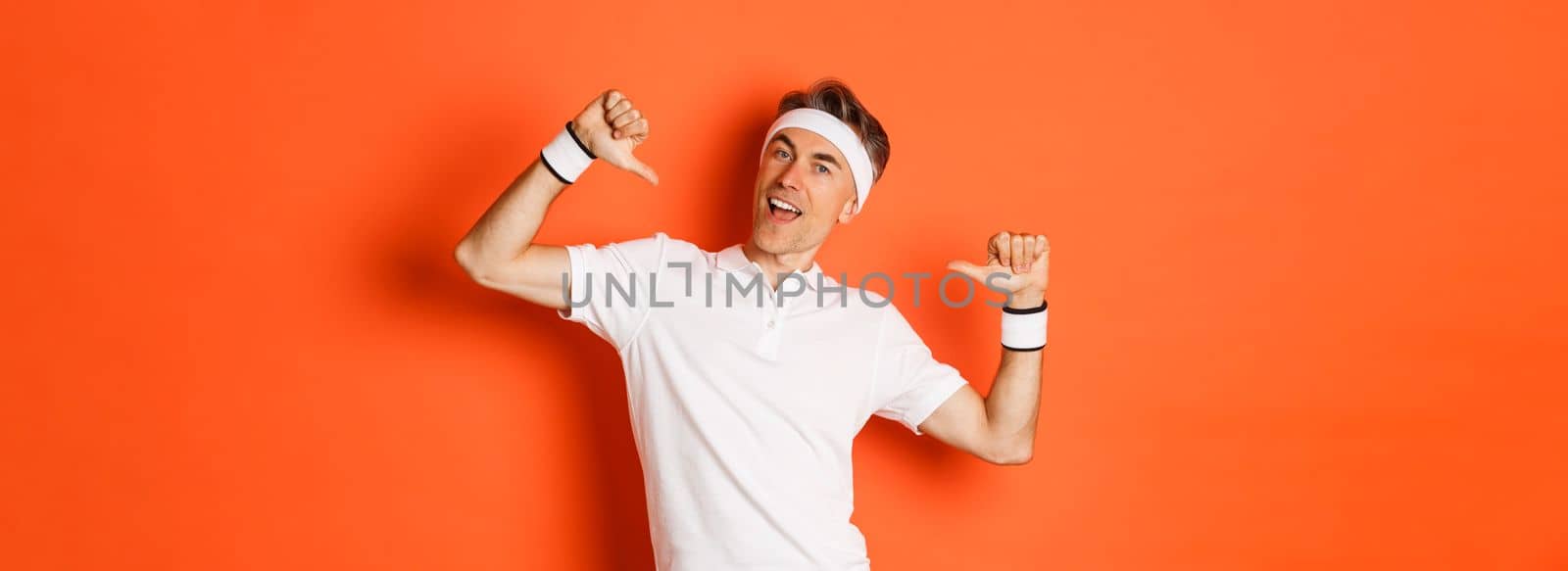 Concept of sport, fitness and lifestyle. Image of confident middle-aged man pointing at himself proudly, wearing clothes for workout, standing over orange background by Benzoix