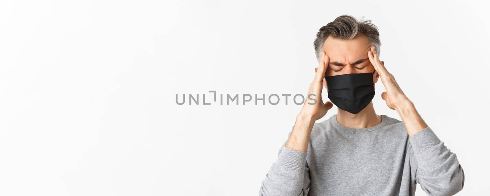 Concept of covid-19, social distancing and quarantine. Close-up of middle-aged man in medical mask, feeling sick or dizzy, touching head, suffering headache or fever from coronavirus by Benzoix