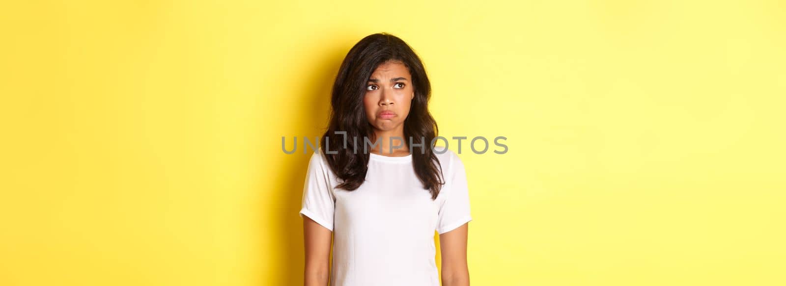 Portrait of sad and disappointed african-american woman, sulking and frowning as looking at upper left corner, see something upsetting, standing over yellow background by Benzoix