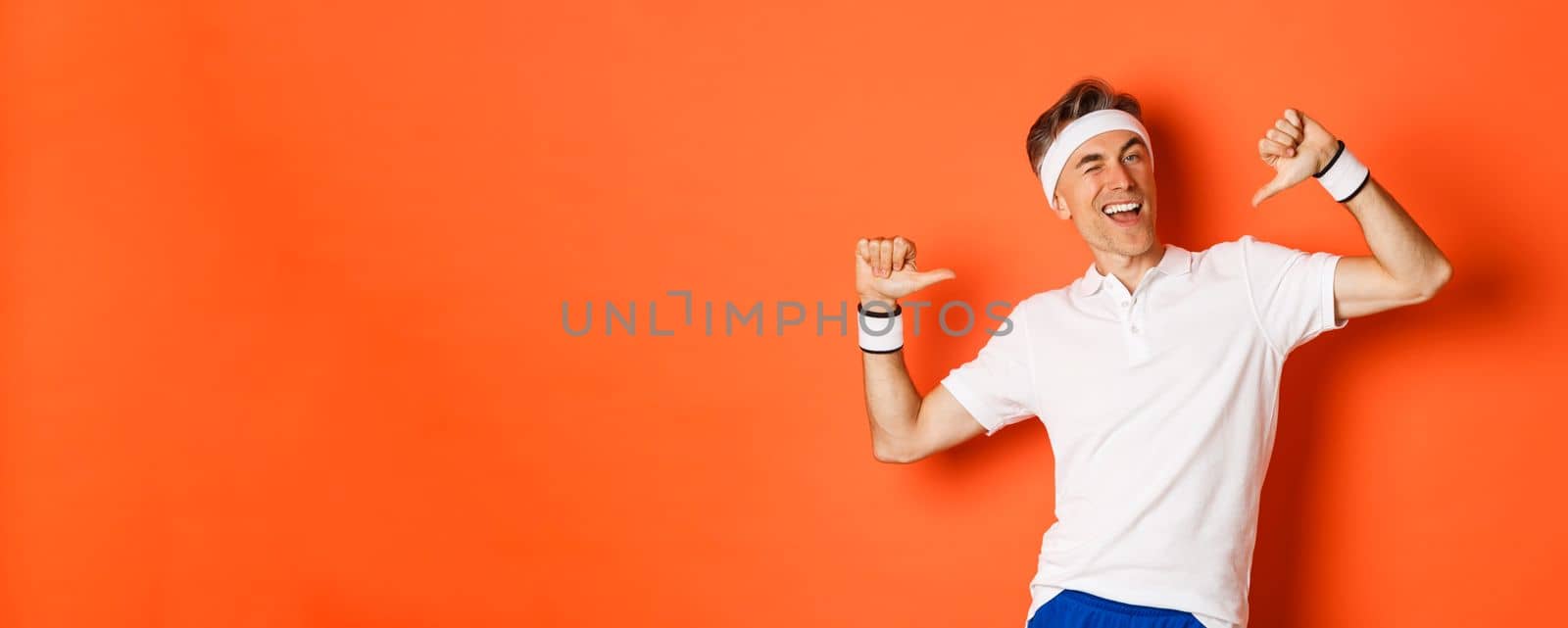 Concept of sport, fitness and lifestyle. Image of confident middle-aged man pointing at himself, bragging about achievement, wearing clothes for workout, standing over orange background.
