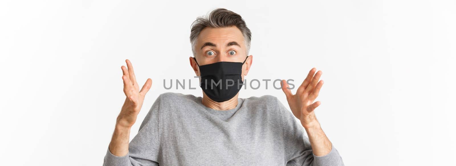 Concept of covid-19, social distancing and quarantine. Close-up of handsome middle-aged man in black medical mask, describe something amazed, looking fascinated at camera.