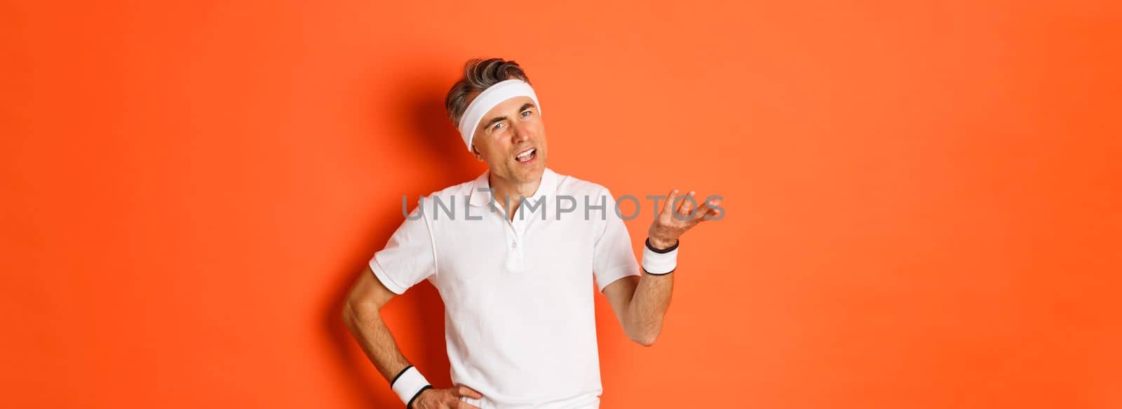 Concept of sport, fitness and lifestyle. Portrait of confused caucasian male athlete, asking question and looking bothered, cant understand something, standing over orange background.