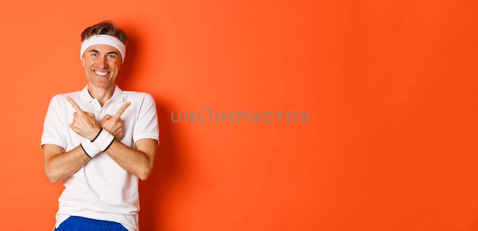 Concept of sport, fitness and lifestyle. Portrait of happy, handsome middle-aged guy in workout clothes, pointing fingers sideways, showing left and right promo banners, orange background by Benzoix