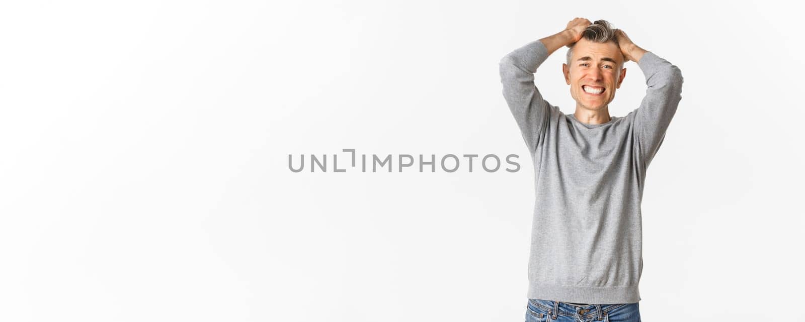 Image of frustrated middle-aged man panicking, losing something, ripping hair on head and grimacing from distress and failure, standing over white background.