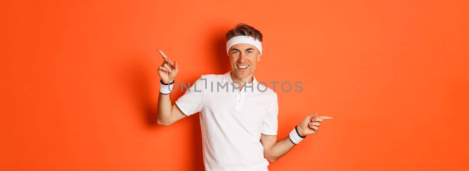 Concept of workout, sports and lifestyle. Portrait of active and healthy middle-aged guy in sportswear, smiling pleased, pointing fingers sideways and showing advertisements.