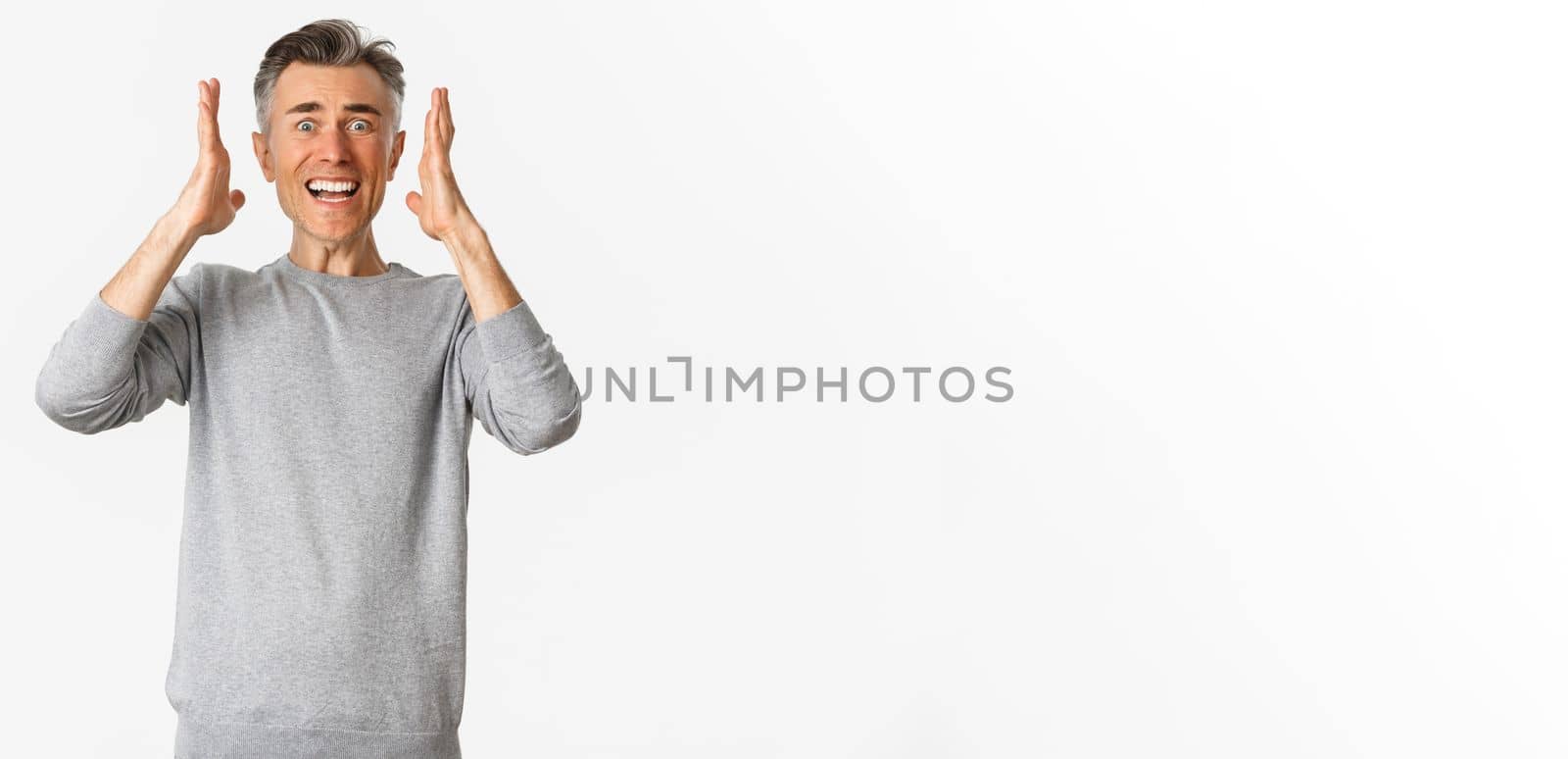 Image of frustrated middle-aged guy in grey sweater panicking, shaking hands and looking distressed, standing over white background.