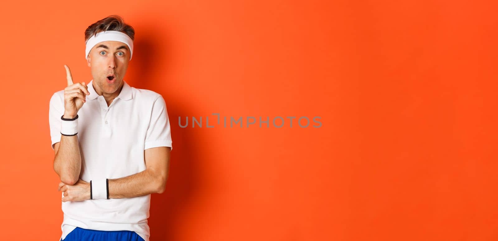 Concept of workout, sports and lifestyle. Portrait of handsome middle-aged male athlete, having an idea, raising finger up and saying suggestion, standing over orange background.
