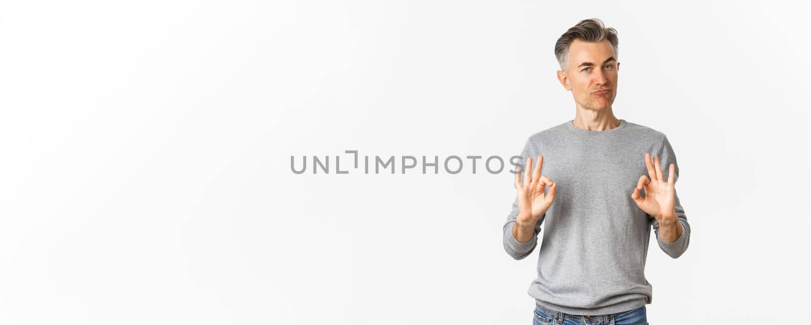 Image of impressed and satisfied middle-aged man, showing okay signs and nodding in approval, praise good choice, standing over white background.