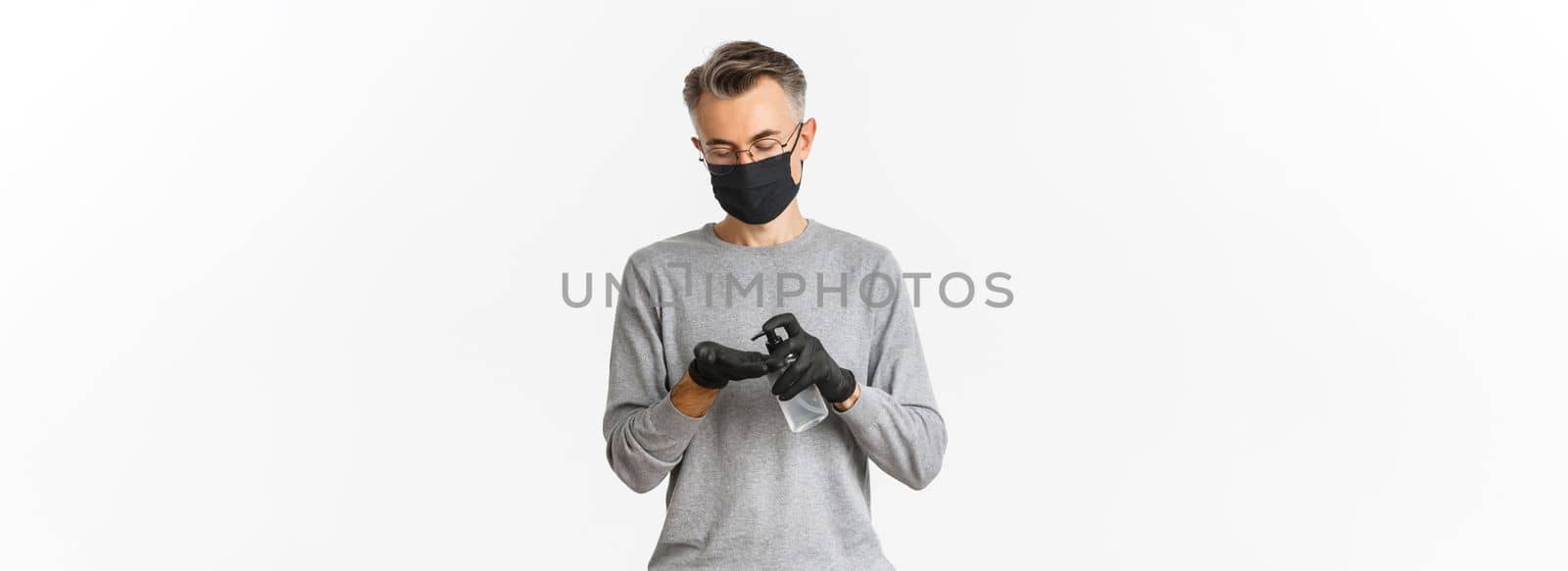 Concept of coronavirus, lifestyle and quarantine. Image of middle-aged man in medical mask and gloves, applying hand sanitizer, preventing catching covid-19, white background.