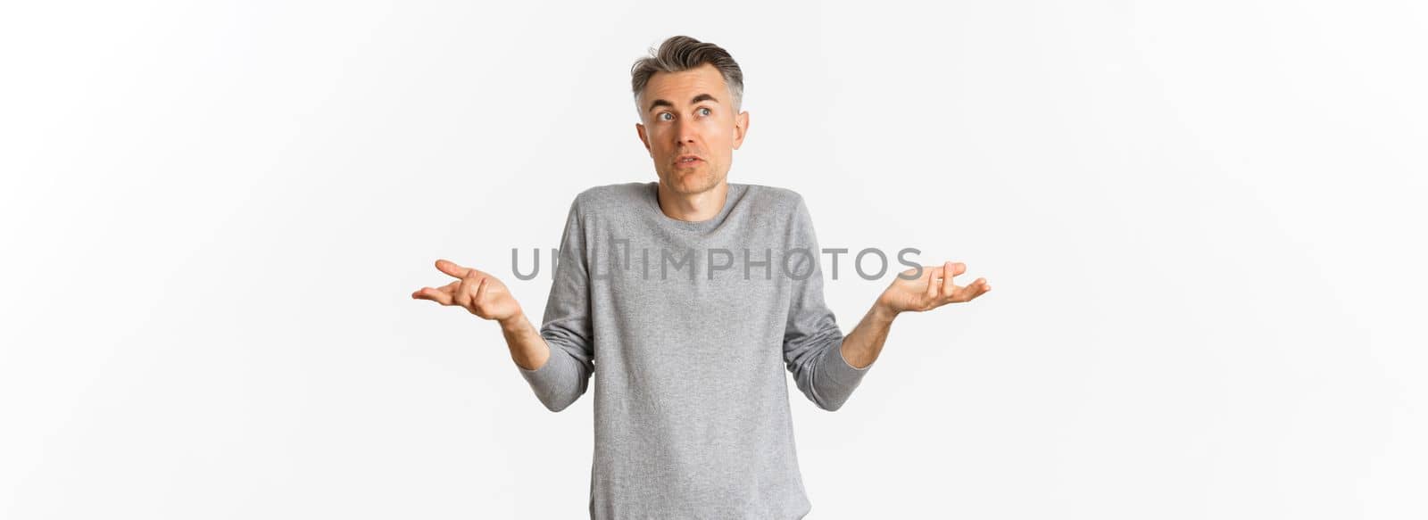 Image of confused middle-aged man with grey hair, shrugging and looking away, cannot understand something, standing over white background.