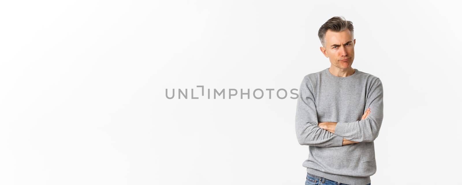 Image of angry and disappointed middle-aged man, being offended or displeased, frowning and grimacing, cross arms on chest, standing over white background.