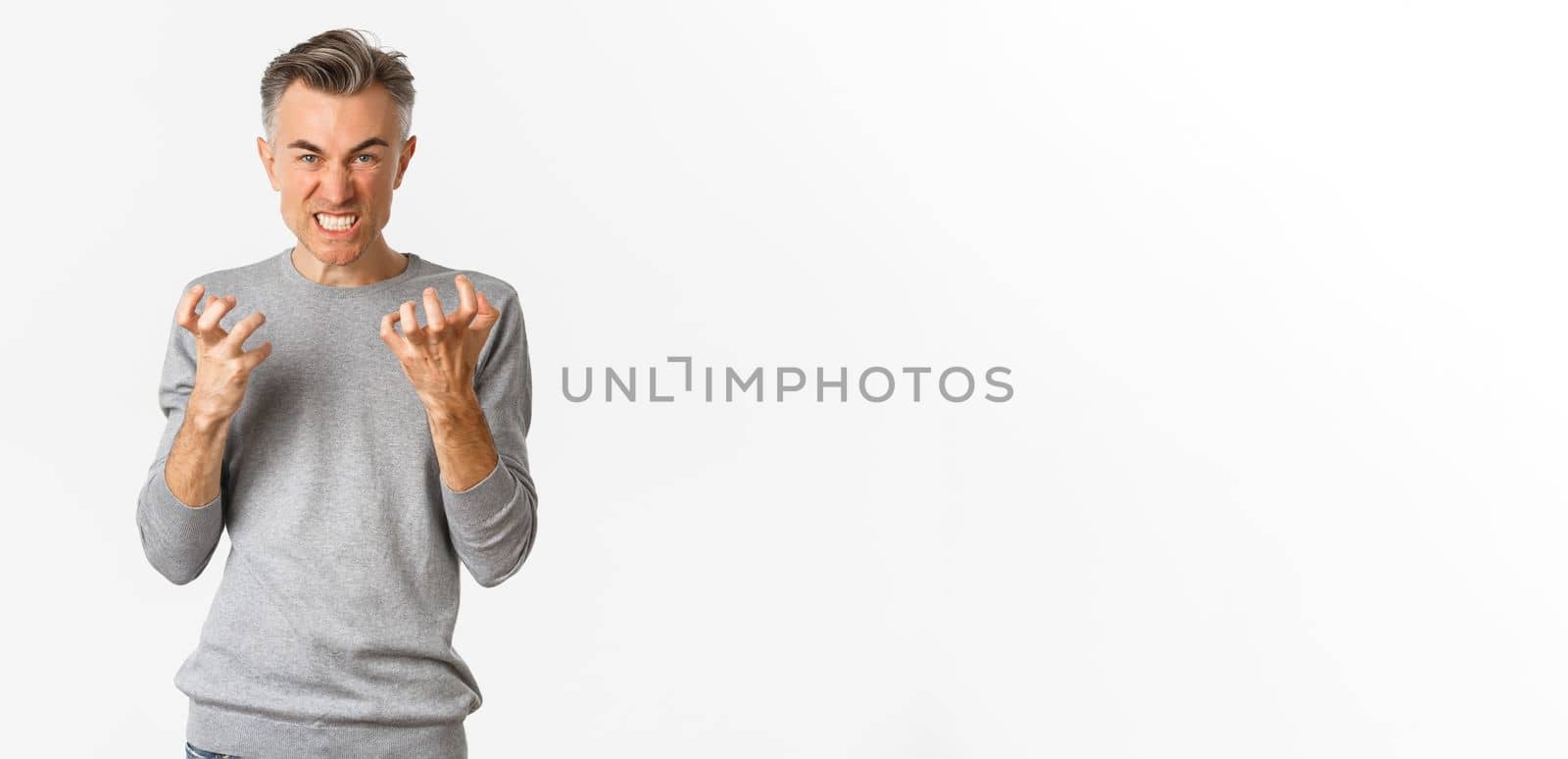 Image of angry middle-aged man cursing someone, looking mad and clenching fists with hatred, standing over white background.