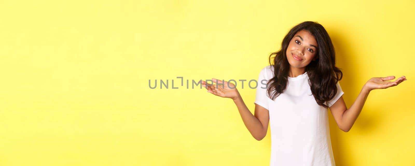 Portrait of clueless, beautiful african-american girl, shrugging and smiling, apologizing for being unaware, standing over yellow background by Benzoix