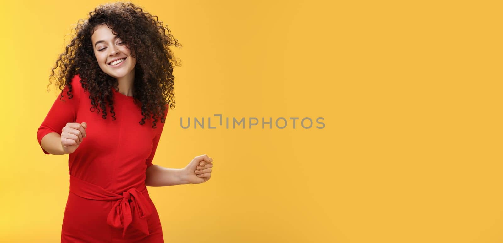 Carefree woman dancing on dance floor with close eyes and smile enjoying life feeling happy and joyful close eyes and making tender expression as moving to rhythm of music over yellow background. People, lifestyle and emotions concept