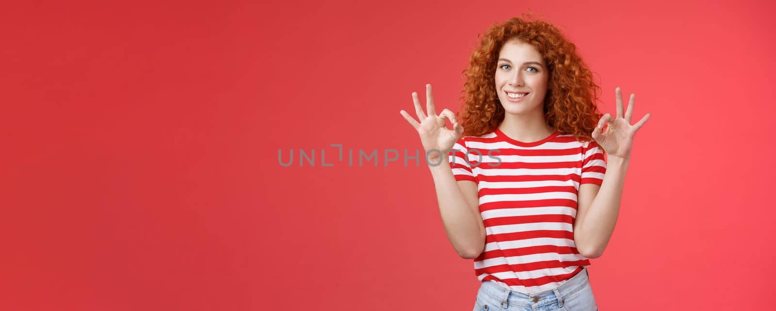 Fine relax everything perfect. Satisfied good-looking redhead cheerful sassy girlfriend curly haristyle show okay ok confirm gesture smiling approval agree good terms stand red background.