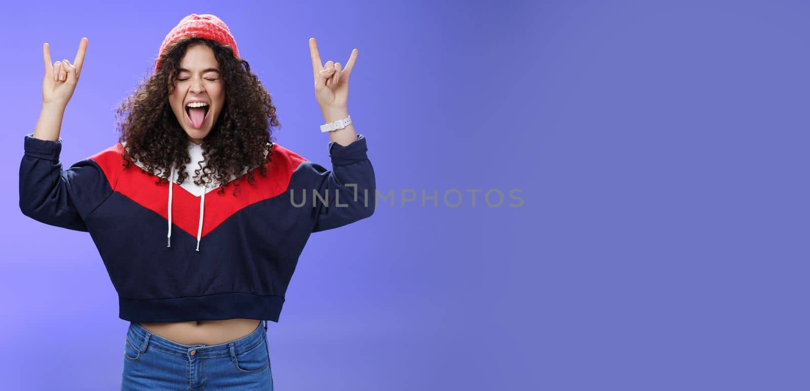 Waist-up shot of rebellious and carefree woman having fun feeling excited and awesome at party close eyes sticking out tongue and showing rock-n-roll signs, wearing beanie and warm clothes by Benzoix