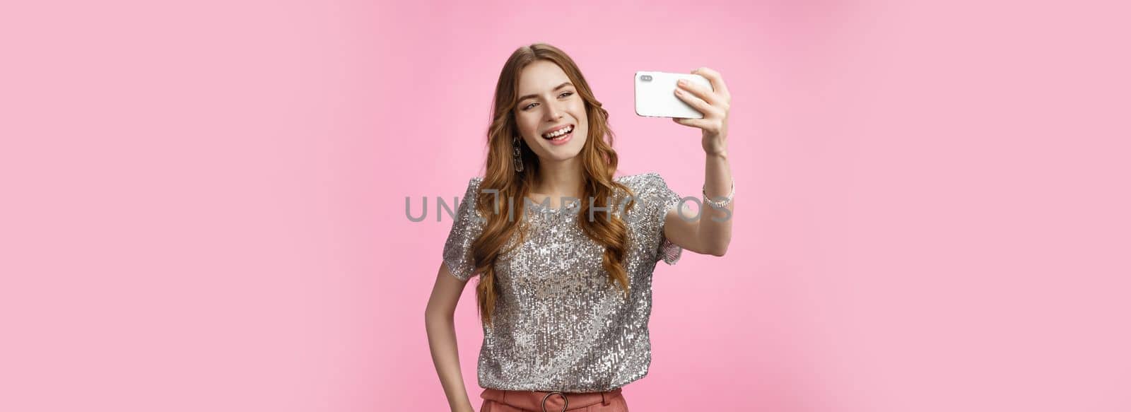 Sociable good-looking confident feminine caucasian woman recording video message taking selfie holding smartphone upper angle capturing image partying send photo online, posing pink background.