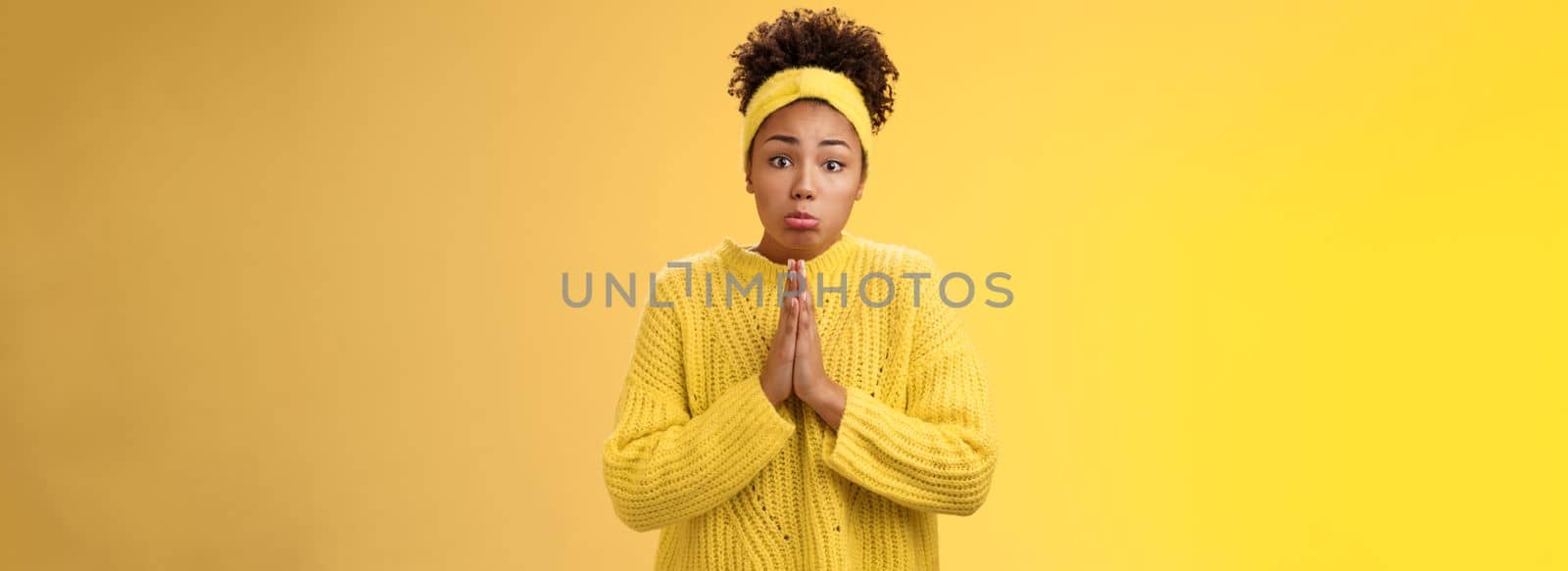 Silly cute pitty young african-american teenage daughter asking pocket money go trip press palms supplication pray need help begging make sad sulking miserable expression, standing yellow background.