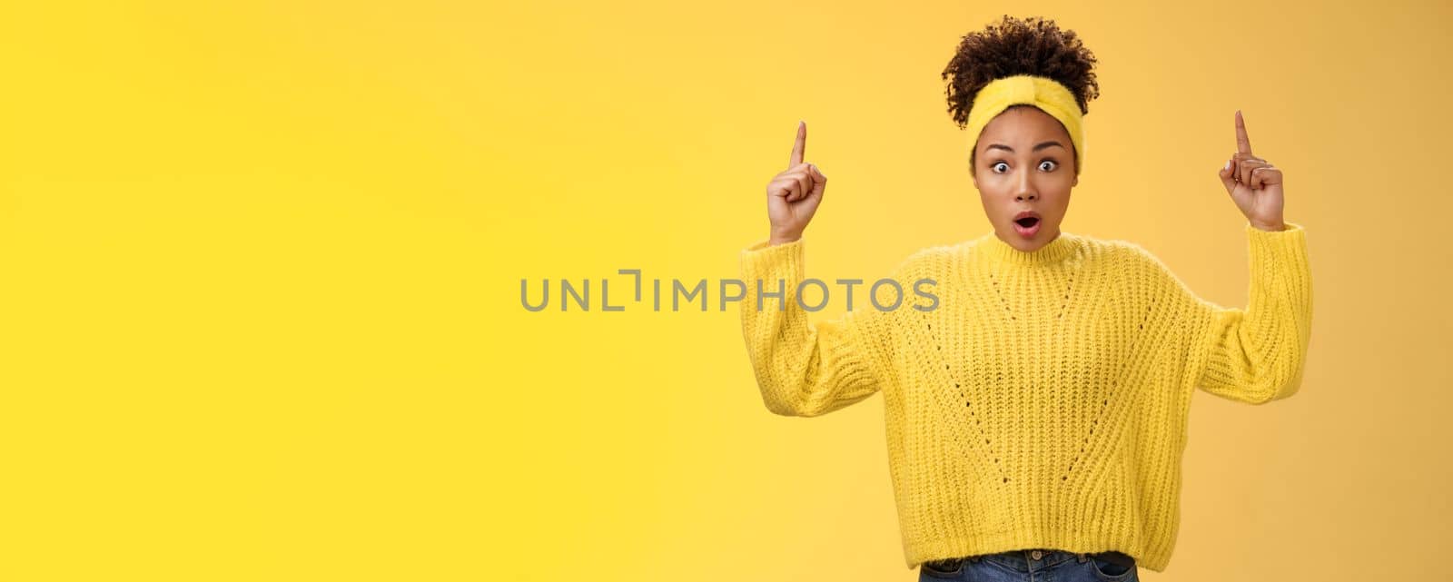 Shocked surprised emotive african-american female student drop jaw widen eyes learn astonishing news pointing raised fingers up gasping concerned impressed, speechless standing yellow background by Benzoix