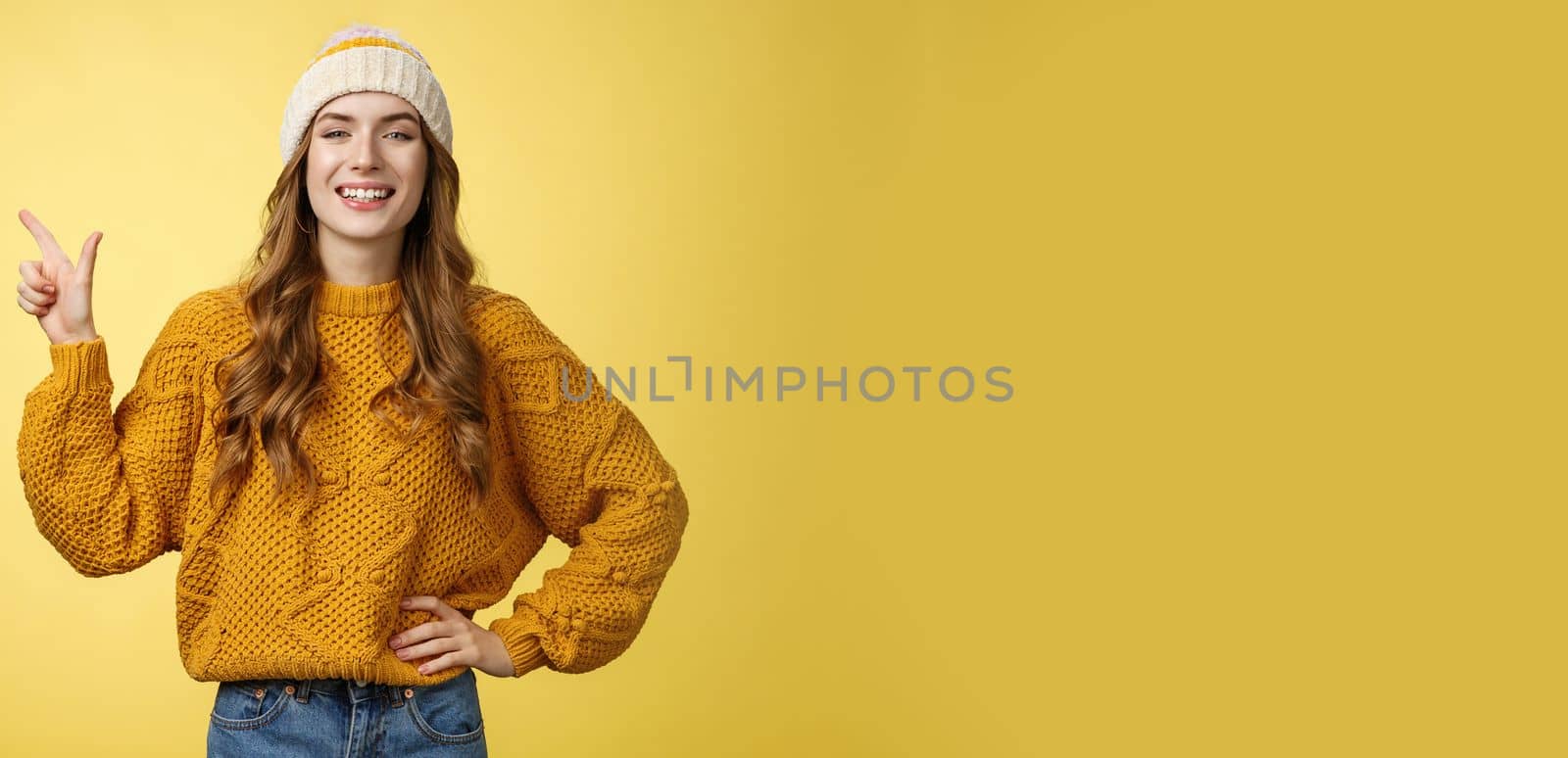 Confident fashionable 20s girl proudly smiling hold hand waist self-assured pointing upper left corner showing perfect copy space top advertisement, promoting product grinning delighted.