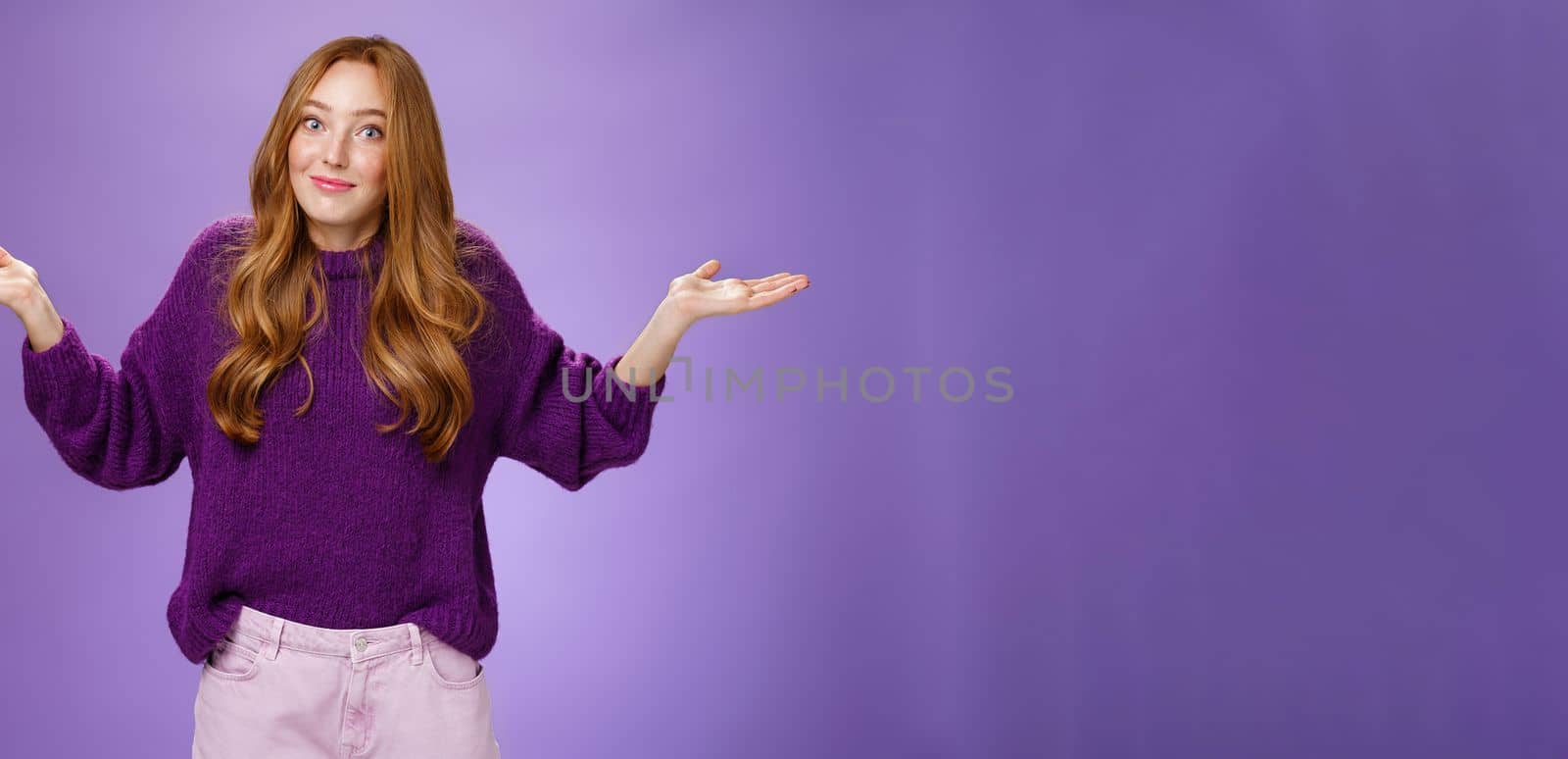 Well who cares, nothing to do. Portrait of funny and careless unbothered chill redhead female shrugging with spread hands and tight smile being unaware and not giving interest over purple background.