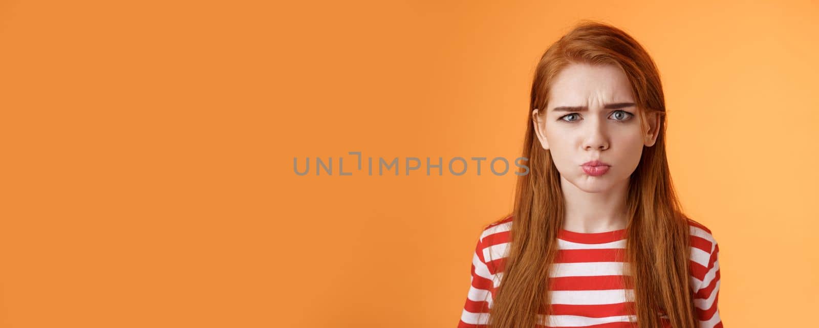 Childish offended cute redhead girl pouting, sulking upset, frowning, complain unfair situation, whining displeased, grimacing upset, act immature demand buy copy space orange background by Benzoix