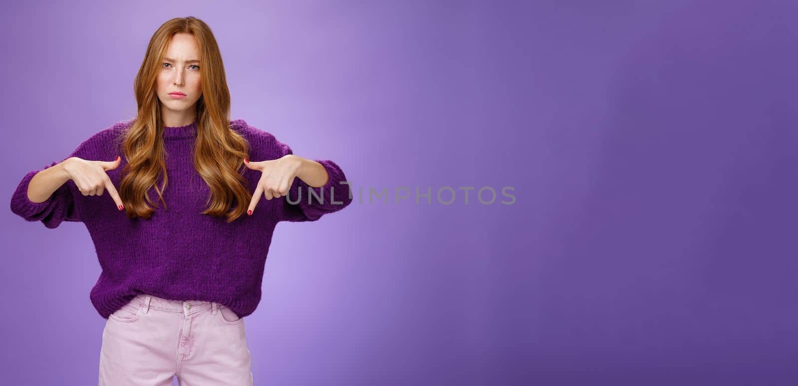 Woman dissatisfied with bad quality of service. Portrait of upset disappointed redhead female frowning and sulking as pointing down demanding explanations of bad product over violet wall by Benzoix